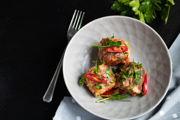 Cod filet or other fish on a gray plate. Braised in tomato and onion. Peas are sprinkled with green leaves and microgreen from seedlings. On a black wooden background.
