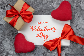 Greeting card with gift box and red bow and heart on concrete background with greeting on...