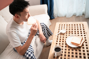 asian young man eat breakfast in living room on sofa