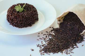Close up of riceberry rice in white plate and in wooden cup with white background.