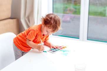 A child sits at a table and draws green watercolors paints. Baby art