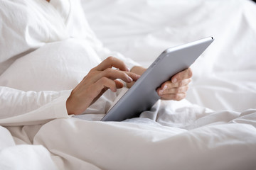 Close up woman holding tablet pc, sitting in bed