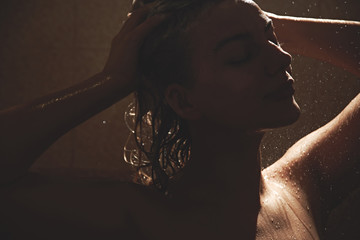 Beautiful satisfied European woman washes away shampoo from the head hair in bathroom, takes a...