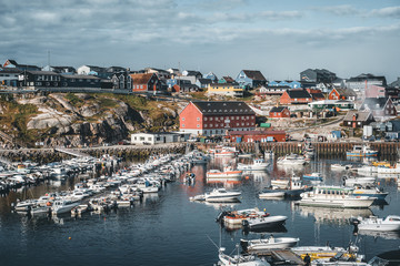 Panoramic view of the port and harbour of Ilulissat, west Greenland. Small local fisher boats with buildings in background. Blue sky with sunny weather
