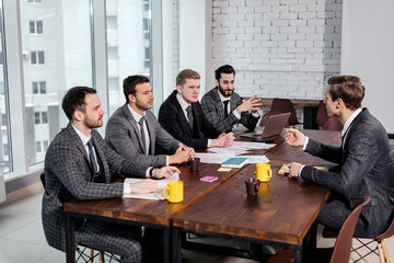 young caucasian manager or boss in tux talk with co-workers, business coworking of stylish elegant men gathered together, have successful interaction in modern executive boardroom