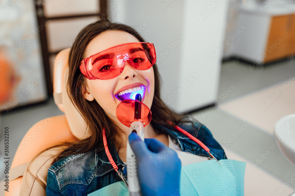 Wall mural dentist ultraviolet light checking up the teeth of a young caucasian woman.