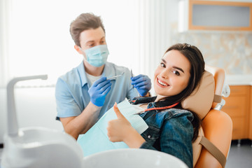 Portrait of dentist in blue mask working with happy patient teeth in modern clinic.