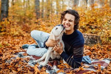 Photo of handsome man and his  labrador playing together in the autumn forest.