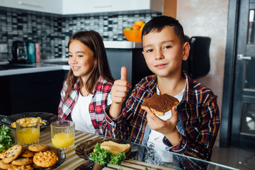 Portrait of two children sit with  fresh juice and bread with chocolate,  looking at camera while...