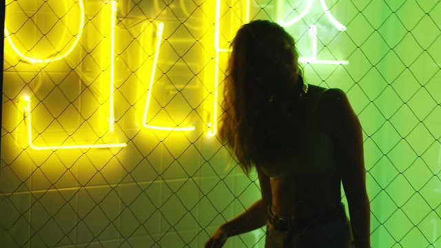 silhouette of sexy girl in dark interior against colourful neon light. Attractive woman in the nightclub moving head with flaying hair while dancing at illuminated background. Nightlife concept