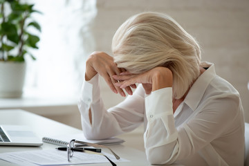 Middle-aged businesswoman lowered head over workplace desk feels unhealthy
