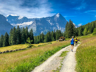 Fototapeta na wymiar Scenic view of Swiss Alps, single cottage house at the foot of the alpine, marathon runner on the pathway in Grindelwald, Switzerland