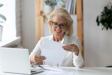 Mature businesswoman holding letter reading paper document feels satisfied