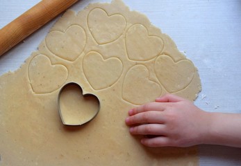 Child's hand makes heart shaped cookies from dough