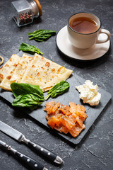 Delicious breakfast - crepes with smoked salmon, spinach and sour cream on stone background.