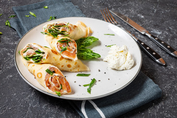 Delicious breakfast - crepes with smoked salmon, spinach and sour cream on stone background.
