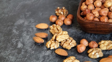 different types of nuts around a wooden dish with hazelnuts on a black background