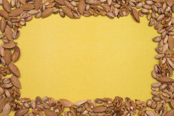 A variety of dried nuts lies on a yellow textured paper background. Peeled walnuts, pistachios and almonds.
