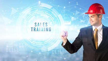 Handsome businessman with helmet drawing SALES TRAINING inscription, contruction business concept