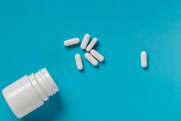 White pills and white plastic medicine bottle on blue background