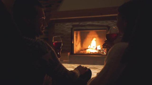 The happy couple sitting by the fireplace and drinking wine