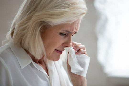 Aged woman holding napkin blows runny nose need antiviral medication