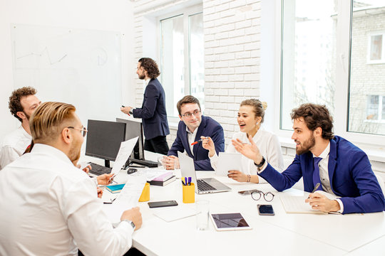 group of young caucasian business leaders gathered in office to discuss projects and ideas together, colleagues sit on table and have friendly conversation, smiling. Business people concept