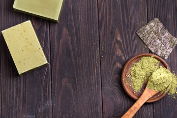Bars of green natural olive oil soaps with green powder and dry seaweed on dark wooden background,