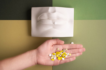Excessive use of pills. Placebo effect. Drug abuse concept. A man holds a handful of pills in his hand. Plaster lips in the background. Symbol.