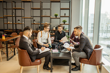 brainstorming time of business team consisted of young successful and confident guys in tuxedo, business crew coworking in modern office, creating and developing business projects