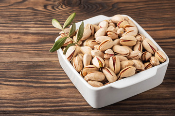 pistachios and leaves in a white plate on a wooden background, copy space