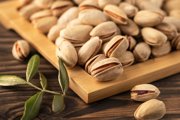 pistachios on a plate, leaves and wooden background, close-up