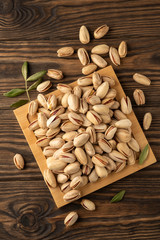 pistachios on a plate, leaves and wooden background, close-up, top view