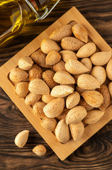 inshell almonds on a wooden background and a bottle of almond oil