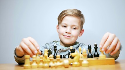 Happy beautiful boy playing chess. Caucasian child thinks while playing chess boardgame. White background                             