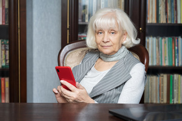 Beautiful old woman reads social networks on his smartphone. She is thinking of gaining more likes and followers. Modern and fashionable woman.