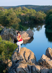Fototapeta na wymiar adult woman doing yoga asanas on the rocks above the river