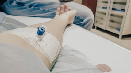 Coronavirus epidemic. Closeup of a hand with a catheter in vein. A woman is lying in a hospital bed. Blood stain on the sheet. Covid-19