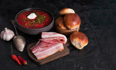 Traditional Ukrainian or Russian red vegetable and meat soup borscht in clay pots with garlic buns and sour cream on a wooden background. Traditional Slavic dish with beets, cabbage, tomatoes.