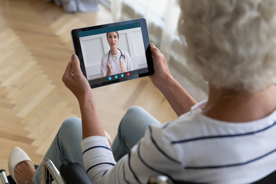 Top view older woman sitting in wheelchair, using computer tablet
