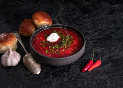 Traditional Ukrainian or Russian red vegetable and meat soup borscht in clay pots with garlic buns and sour cream on a wooden background. Traditional Slavic dish with beets, cabbage, tomatoes.