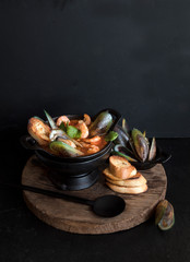 French fish soup Bouillabaisse with seafood, salmon fillet, shrimp on a black background. traditional French cuisine. Copy space