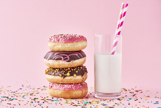 Stack of colorful donuts decorated and glass of milk on a pink background