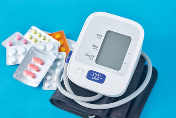 Digital blood pressure monitor and medical pills on a blue background. Healthcare and medicine concept