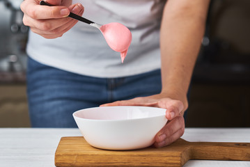Woman whisking red cream for decorating cookies in a bowl on kitchen, closeup