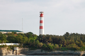 Coastal lighthouse on the edge of a rocky promontory in the black sea, the city of Gelendzhik. Located to the left of the frame. Landscape. Horizontal photo. Blurred background. Summer. opy space