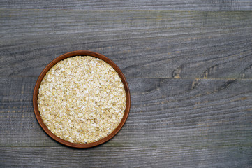 Fototapeta na wymiar Oatmeal flakes in a ceramic brown bowl on an old dark wooden volumetric background.