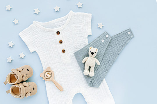 White cotton bodysuit with baby shoes and toys. Set of baby clothes and accessories on blue background. Fashion newborn clothes for summer. Flat lay, top view