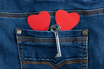 Two red paper hears with a key sticking out of a jean pocket.Valentines day concept.