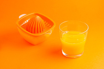 Glass of orange juice and juicer on orange background © Miquel